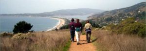 Image of three people hiking on a trail overlooking the ocean.